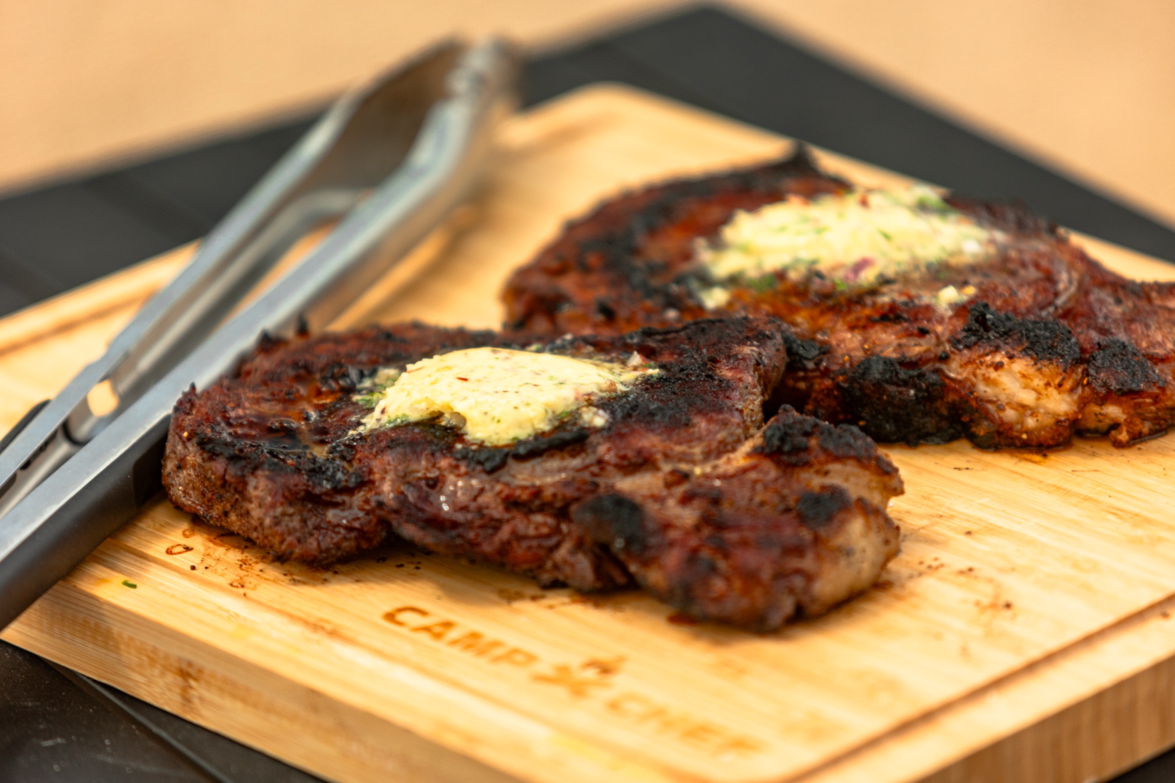 Two seared steaks with herb butter on a cutting board